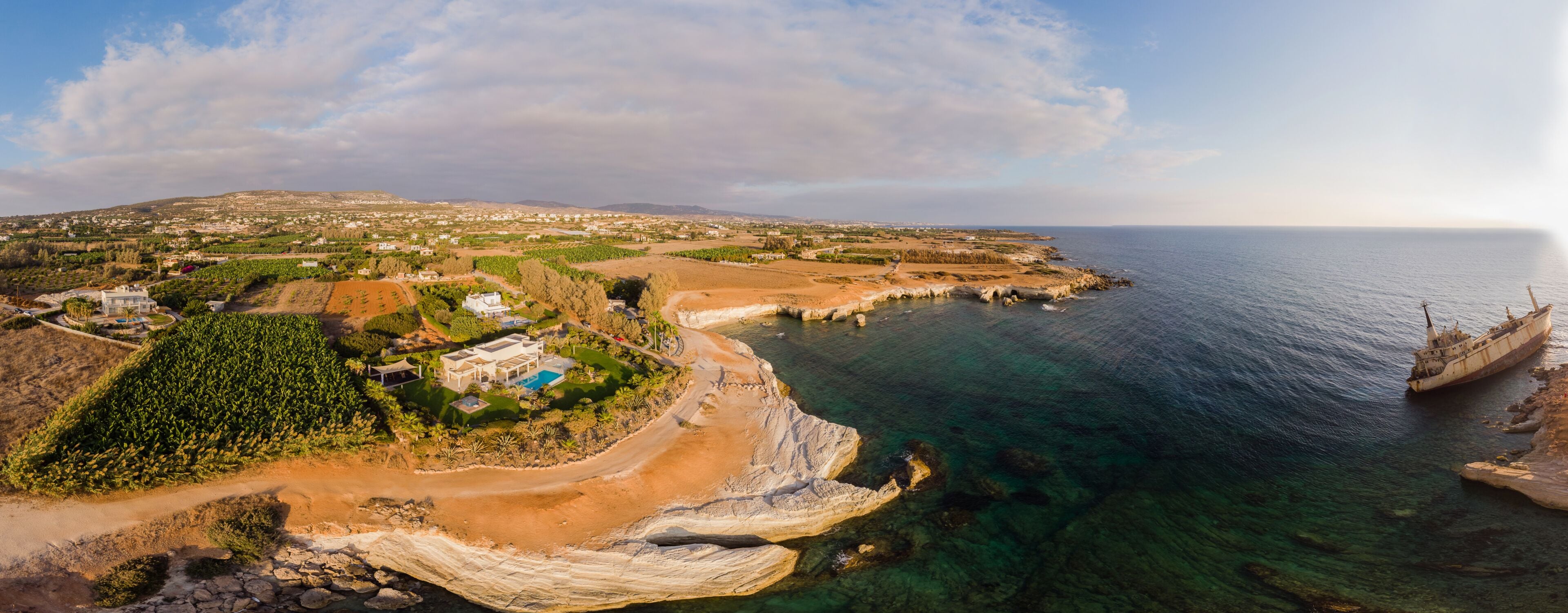 A coastal landscape with a beach, clear waters, and a distant town.