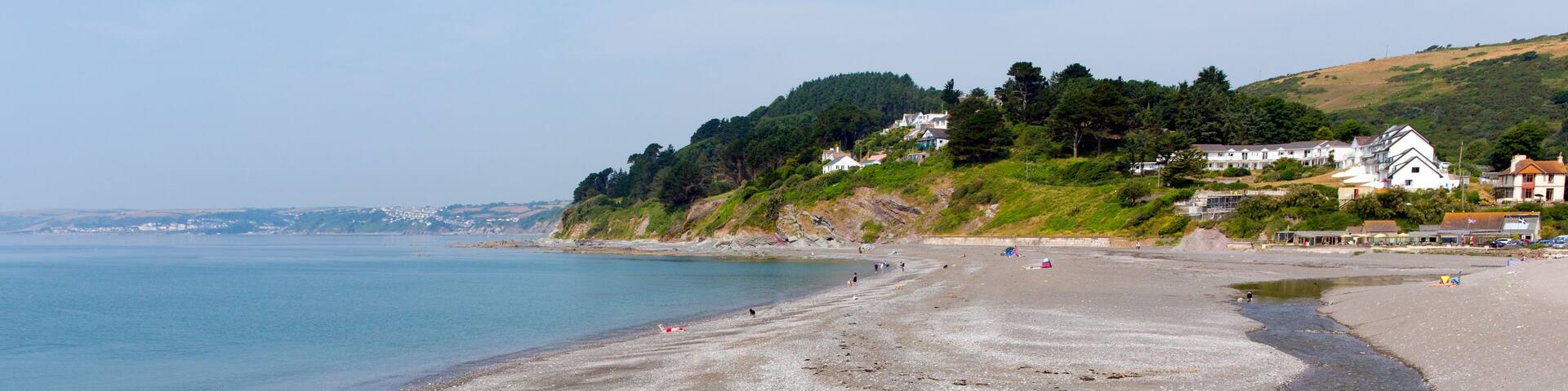 A pebbly beach with houses on a hillside.
