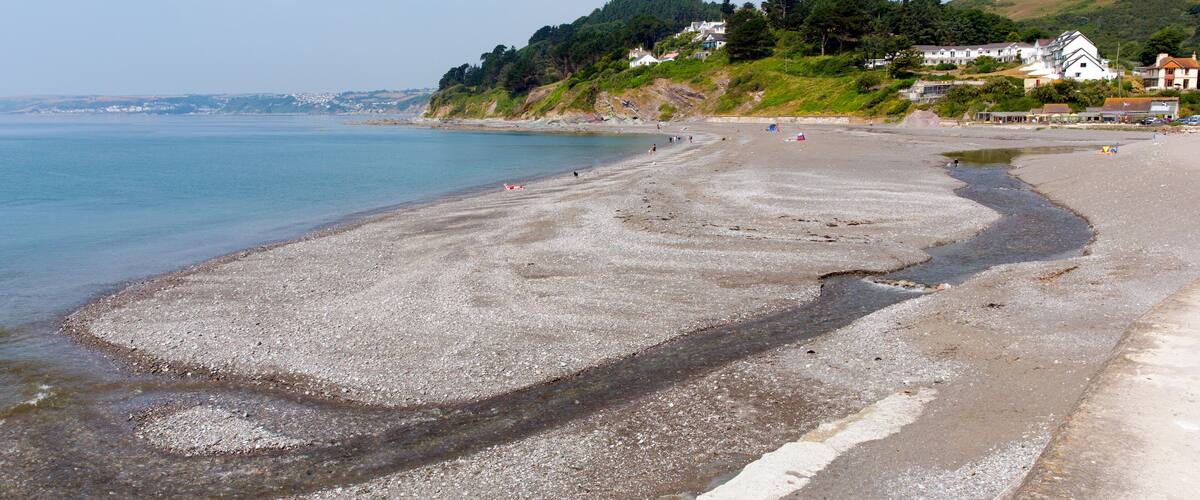 A pebbly beach with houses on a hillside.