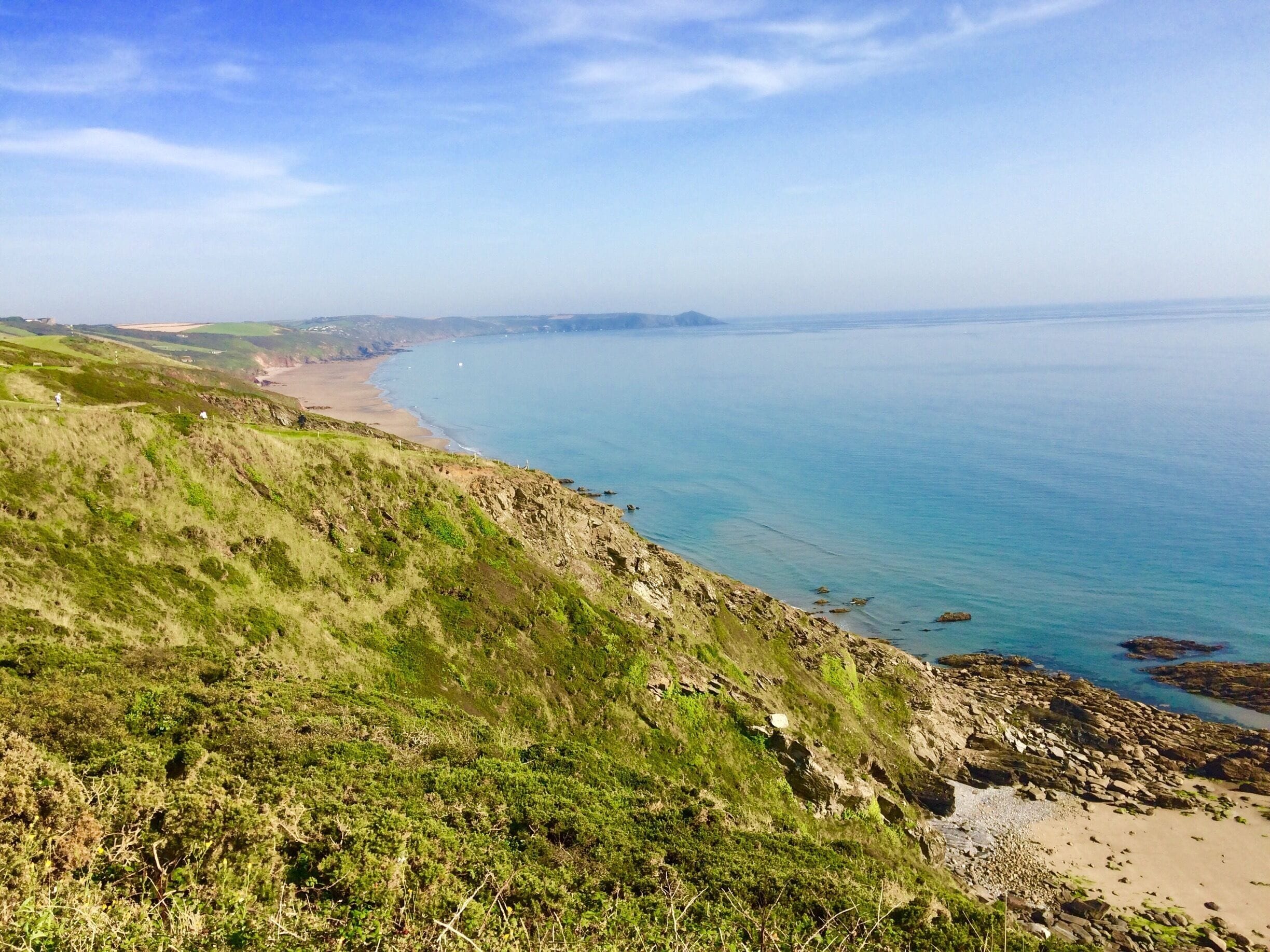 A coastal landscape with grassy hills, a sandy beach, and calm blue waters.