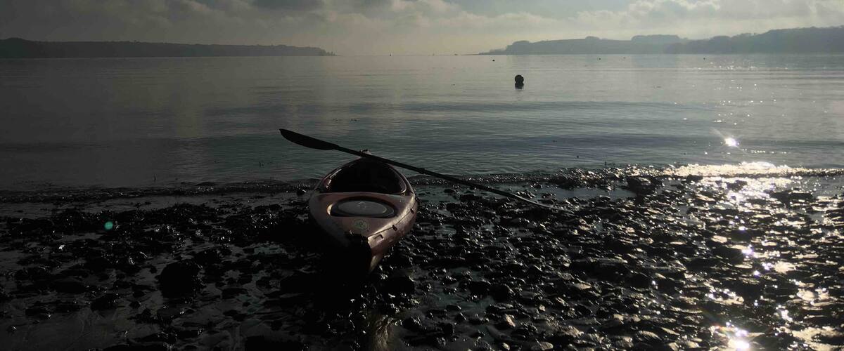 A kayak on a rocky shore with a calm lake and distant land in the background.