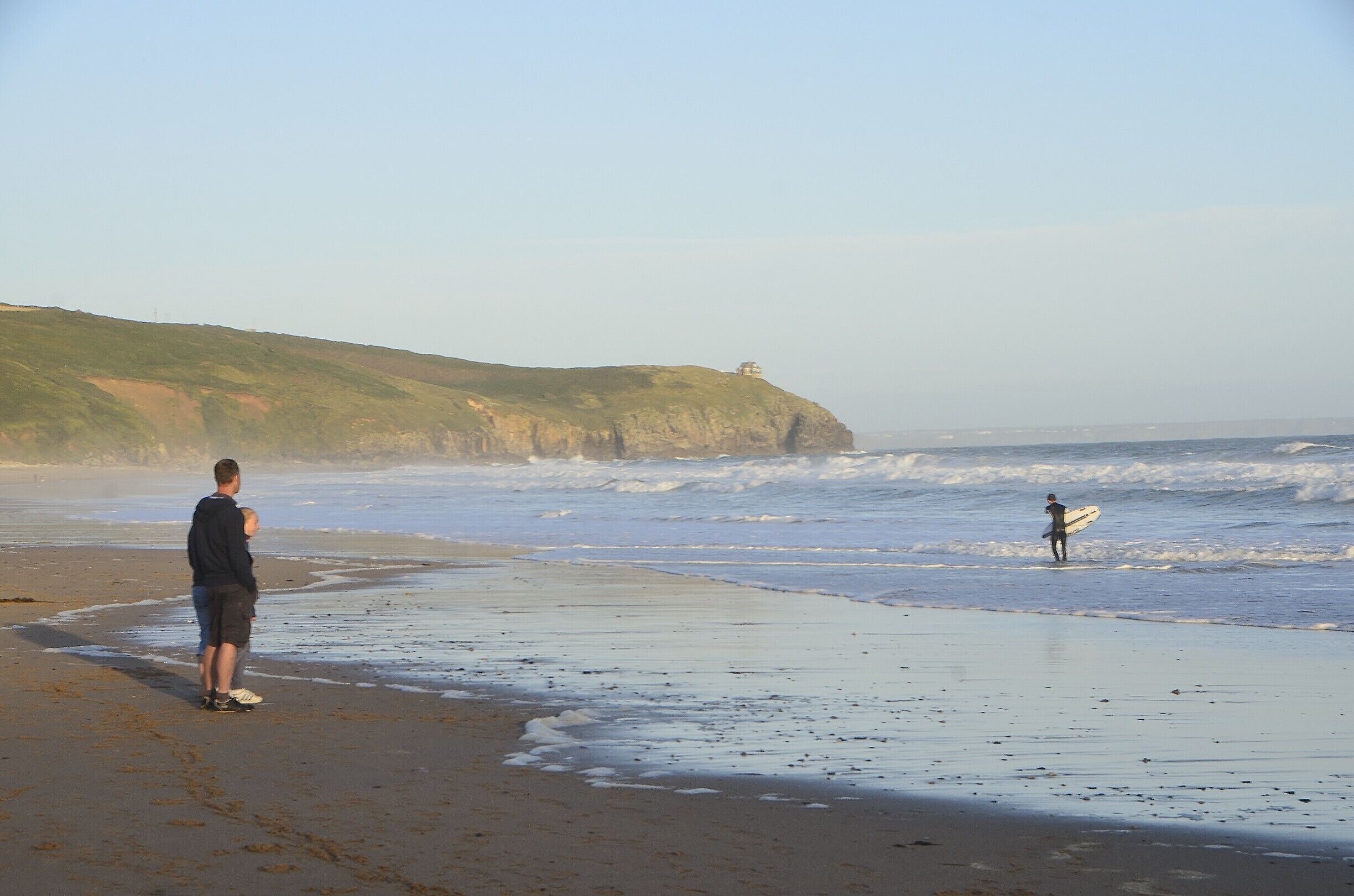 A beach with waves, a cliff, and a person with a surfboard.
