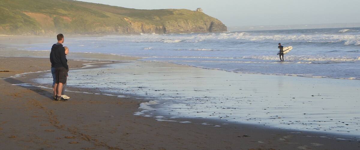 A beach with waves, a cliff, and a person with a surfboard.