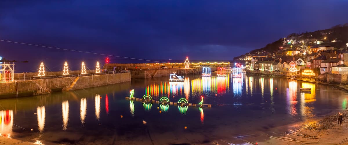 A waterfront at night with illuminated Christmas trees, a bridge, and a town on a hill.