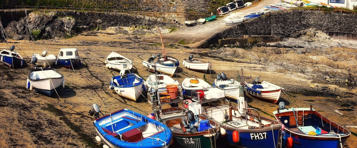 A coastal village with small boats docked on a sandy beach, surrounded by stone walls and houses.