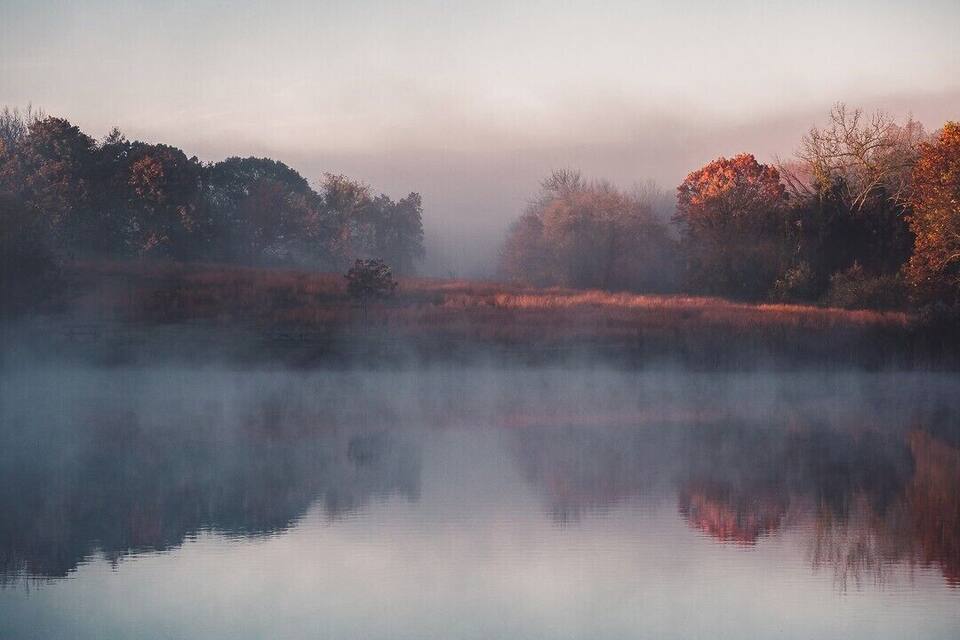 A misty river with autumn-colored trees reflecting on the water.