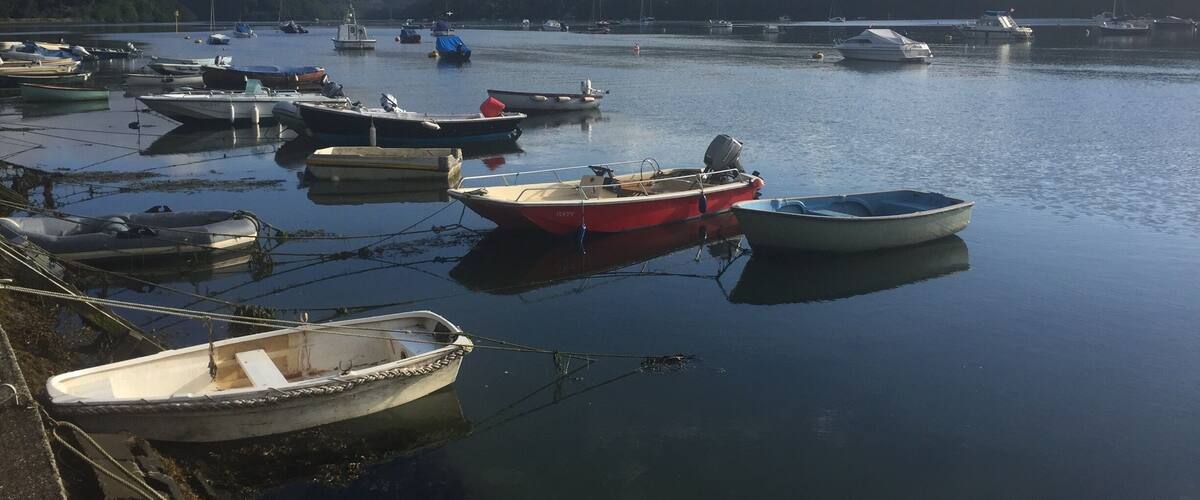A calm harbor with several boats docked, surrounded by hills and a partly cloudy sky.