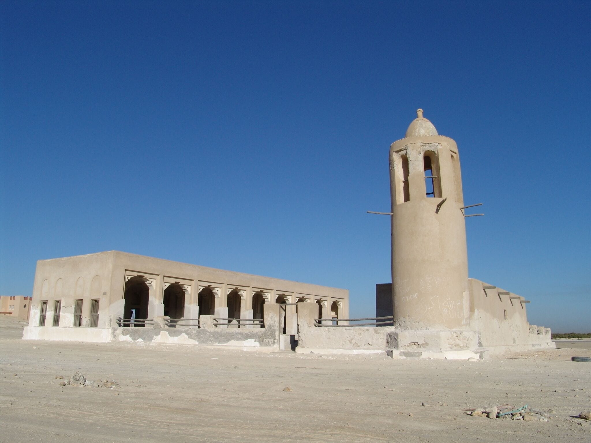 A large, beige, cylindrical tower with a dome on top, surrounded by a building with multiple arches and a flat roof.