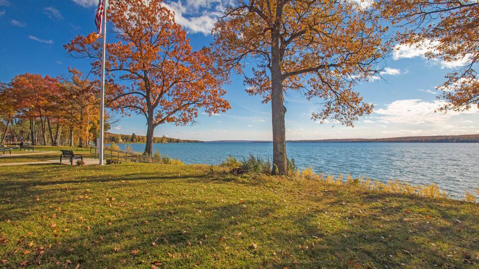 A park with autumn trees, a lake, and a flagpole.
