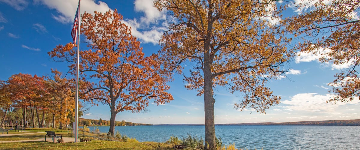 A park with autumn trees, a lake, and a flagpole.
