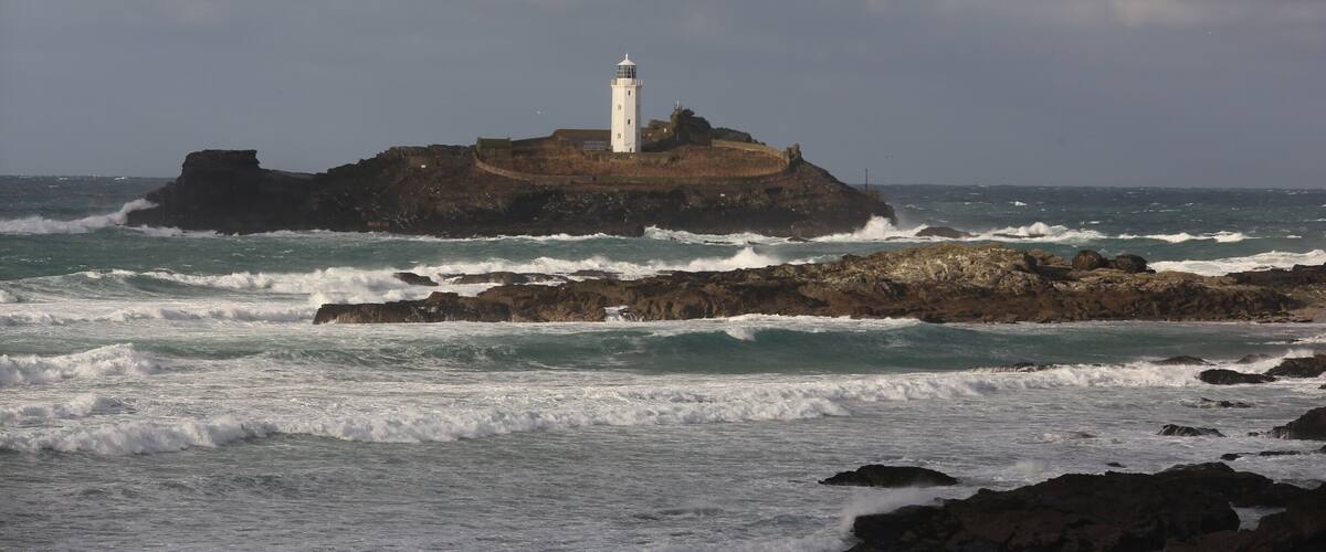 A lighthouse on a rocky island with waves crashing against it.