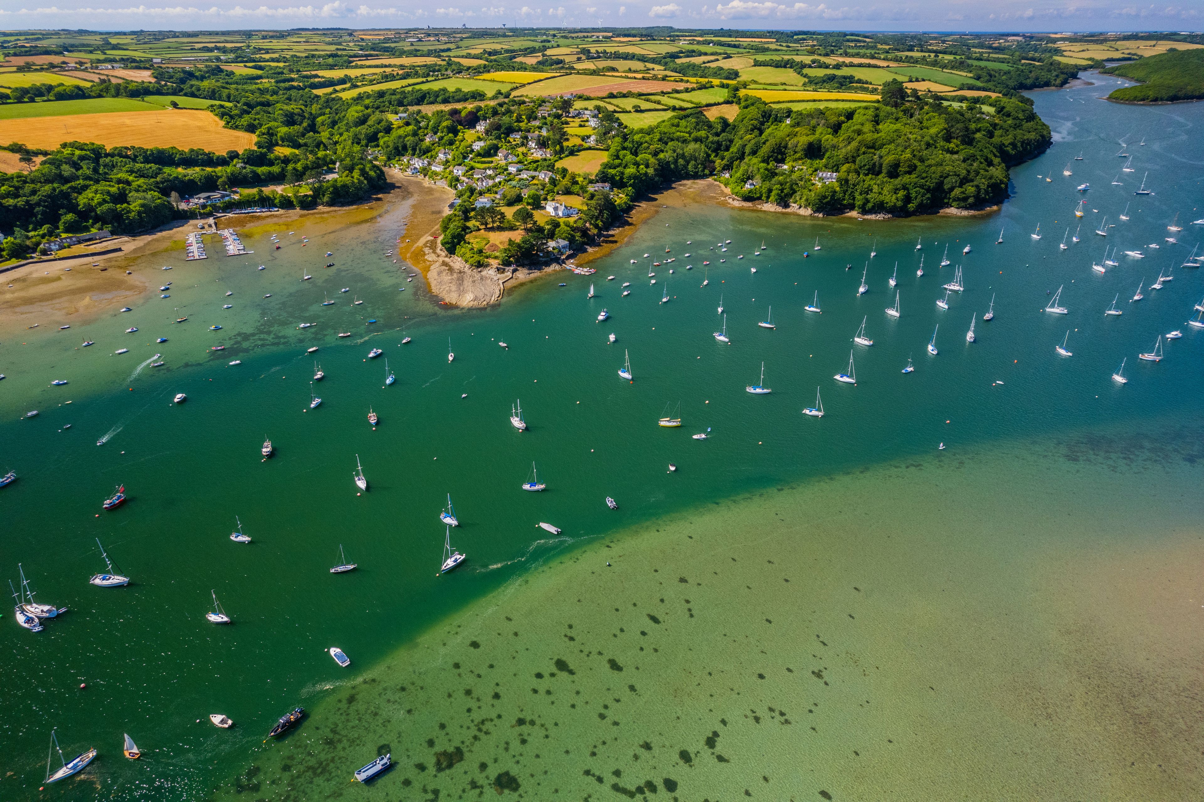 A coastal landscape with a village surrounded by fields and a bay filled with sailboats.