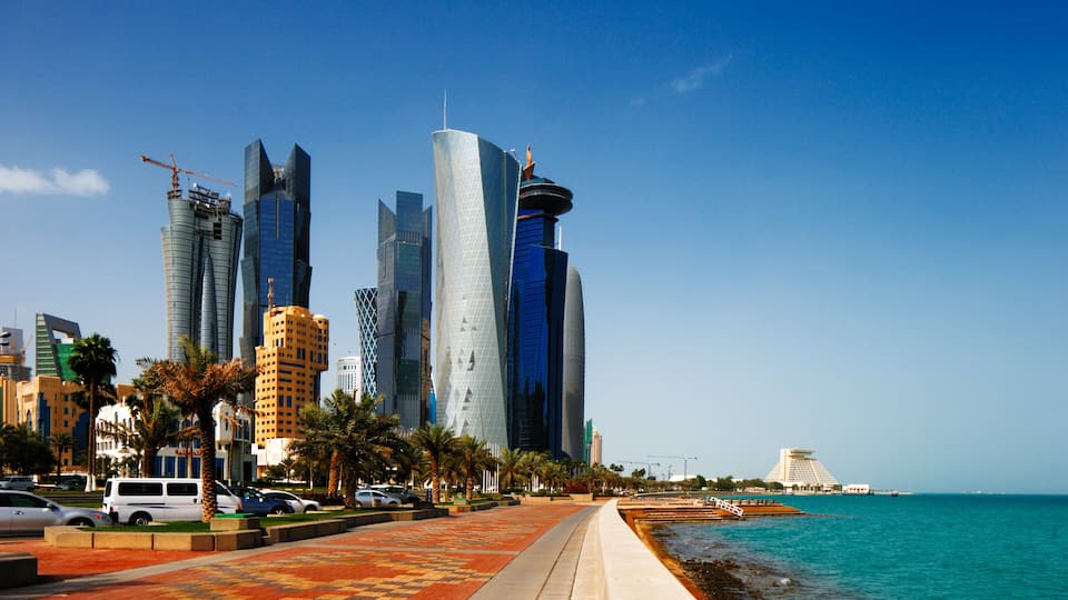A coastal cityscape with modern skyscrapers, palm trees, and a clear blue sky.