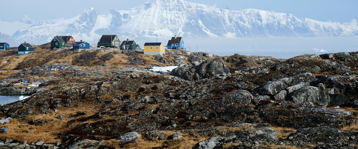 A rugged coastal landscape with colorful houses and a snow-capped mountain in the background.