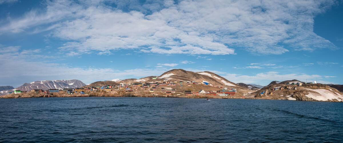 A coastal village with colorful houses, a mountain range, and a clear sky.