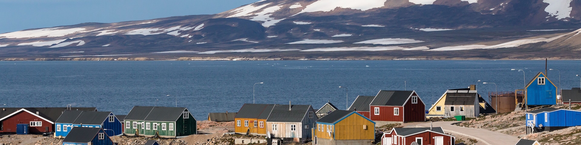 Un pueblo costero con casas coloridas y montañas nevadas al fondo.