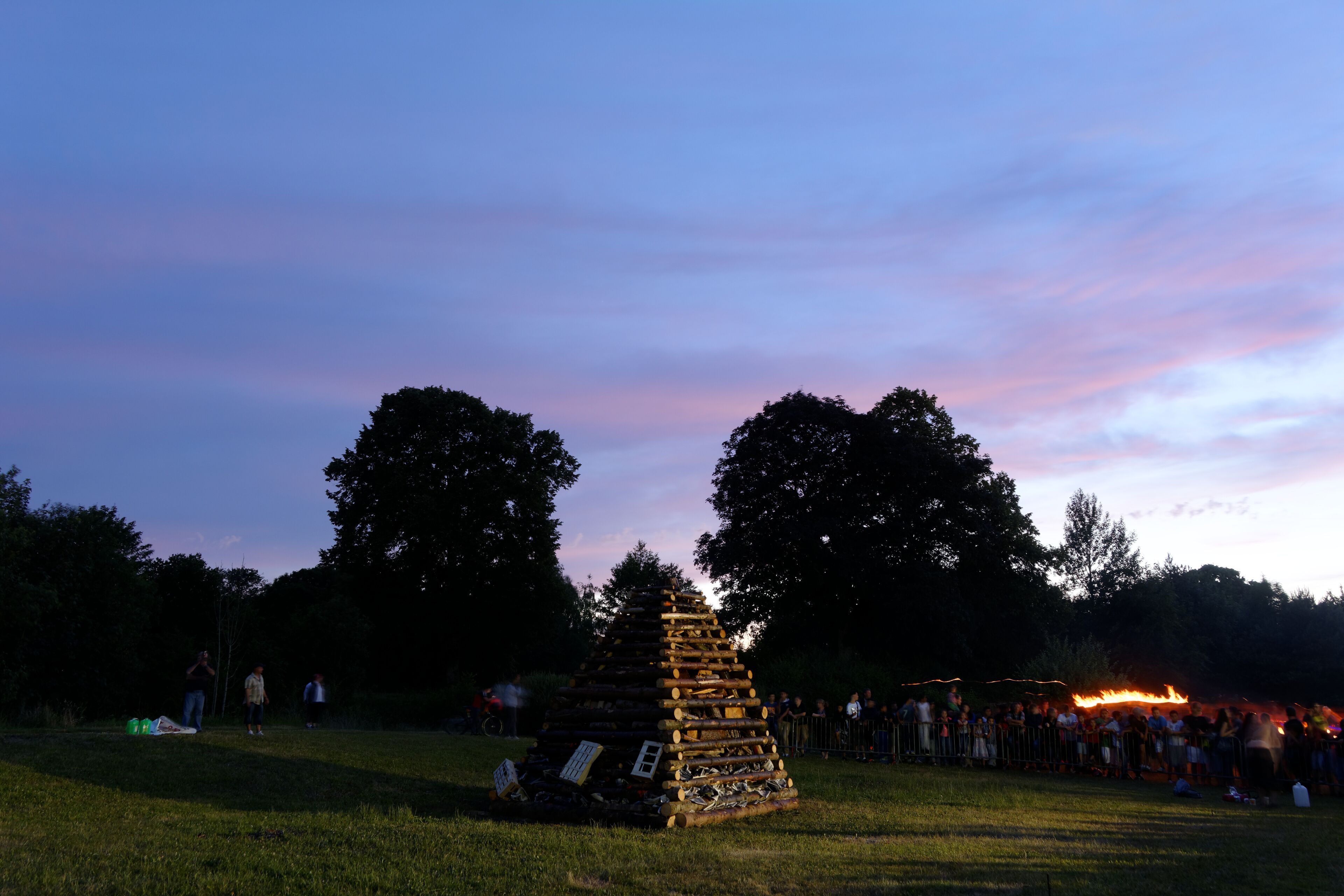 A large pyramid-like structure in a grassy field at dusk with a crowd in the background.