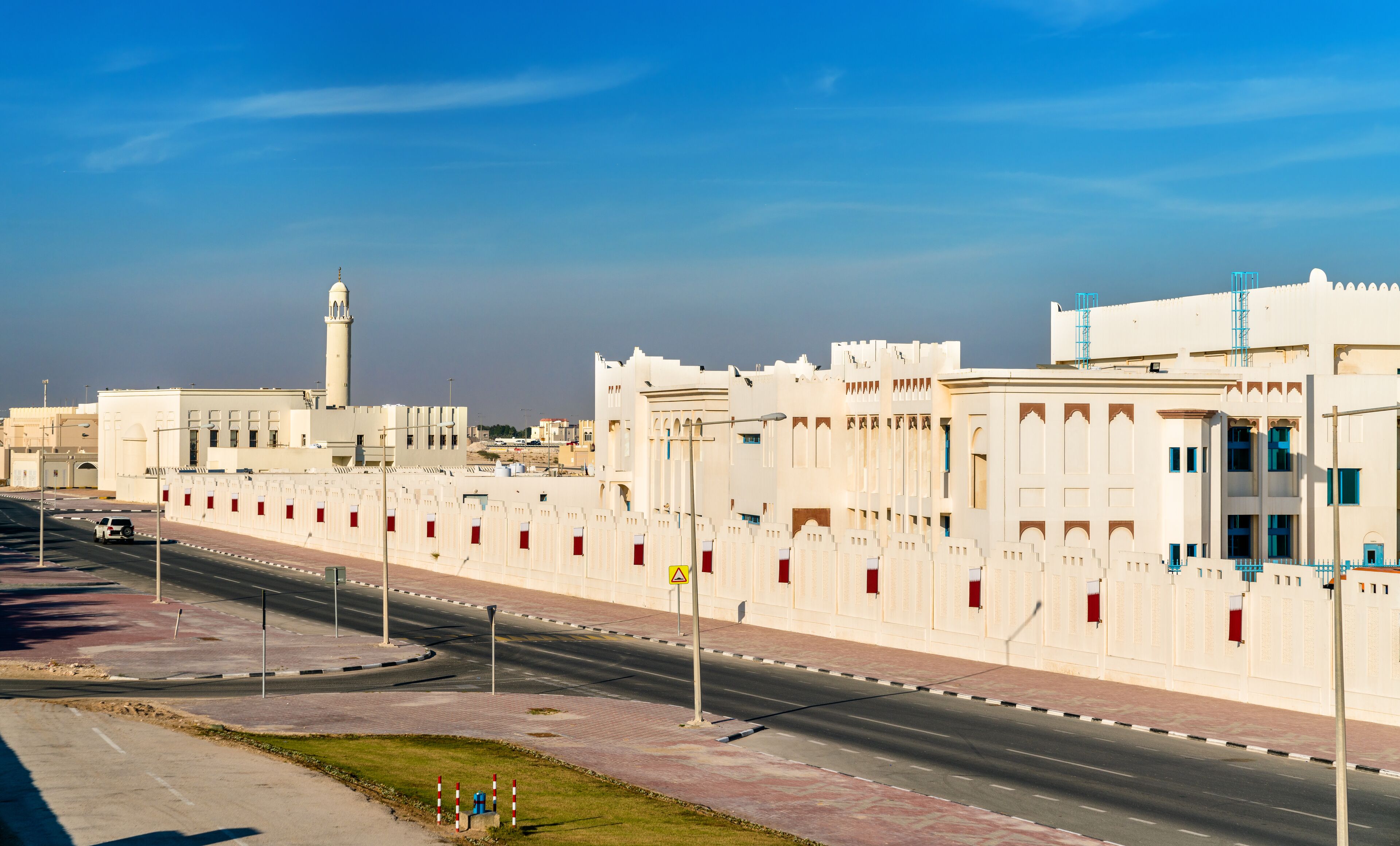 A modern cityscape with white buildings, a road, and a mosque with a minaret.