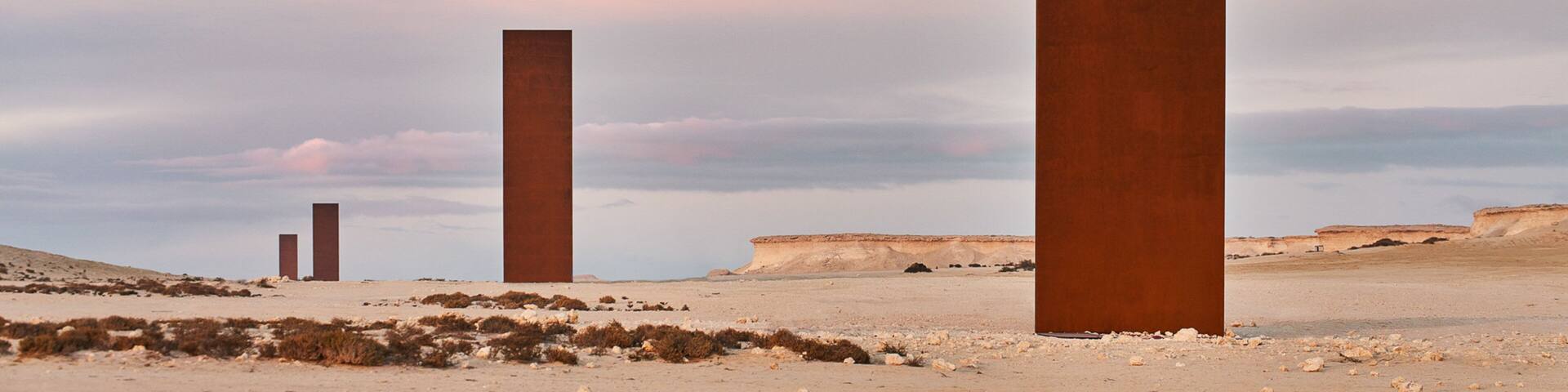 Tres estructuras metálicas altas de color óxido en un paisaje desértico con cielo nublado.