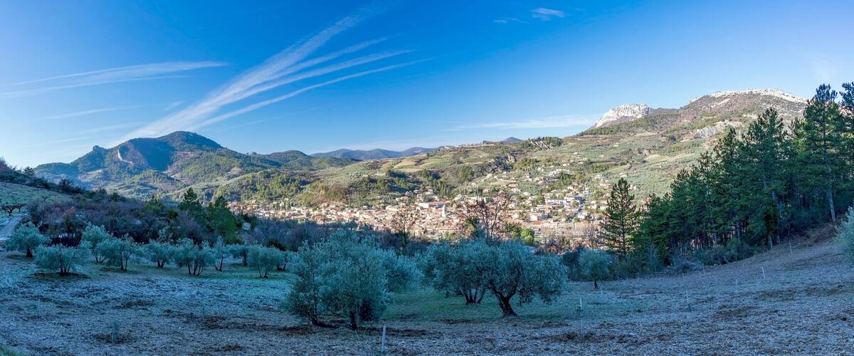 A mountainous landscape with a town nestled in the valley, olive groves, and a prominent rocky peak.