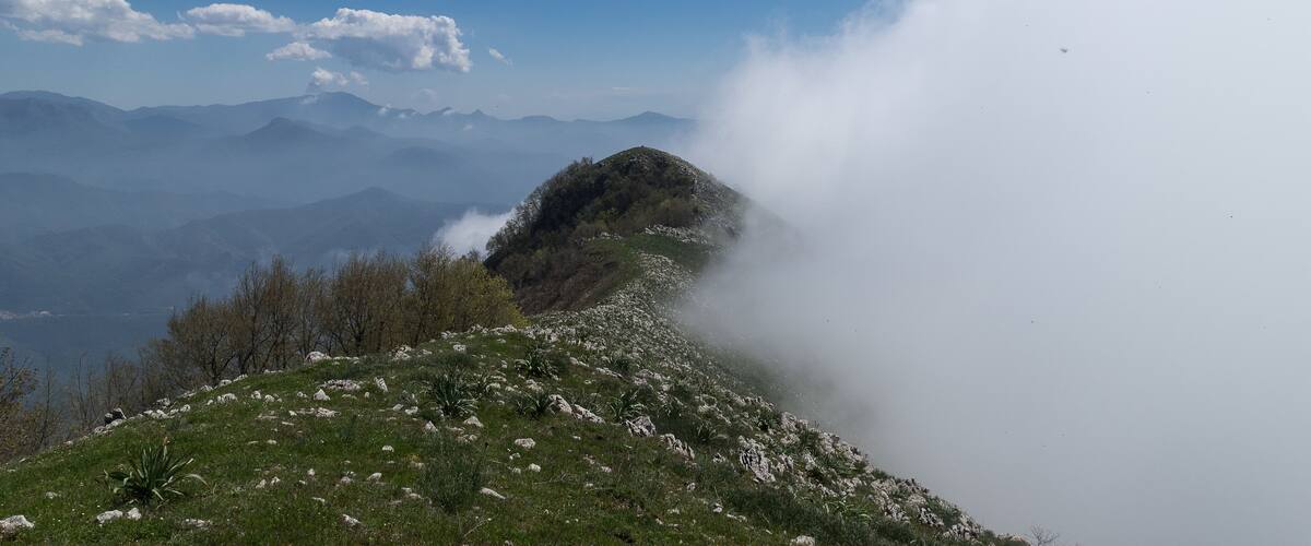 A mountain landscape with a clear sky, distant mountains, and a valley below.