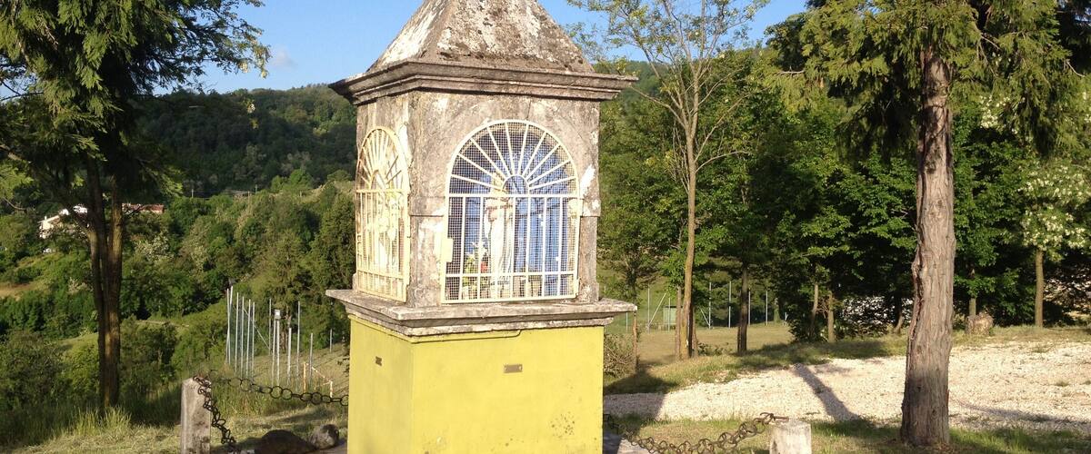 A small, yellow tower with a conical roof and a spherical finial, surrounded by trees and a clear blue sky.