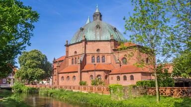 A historic brick building with a green dome and a river in the foreground.
