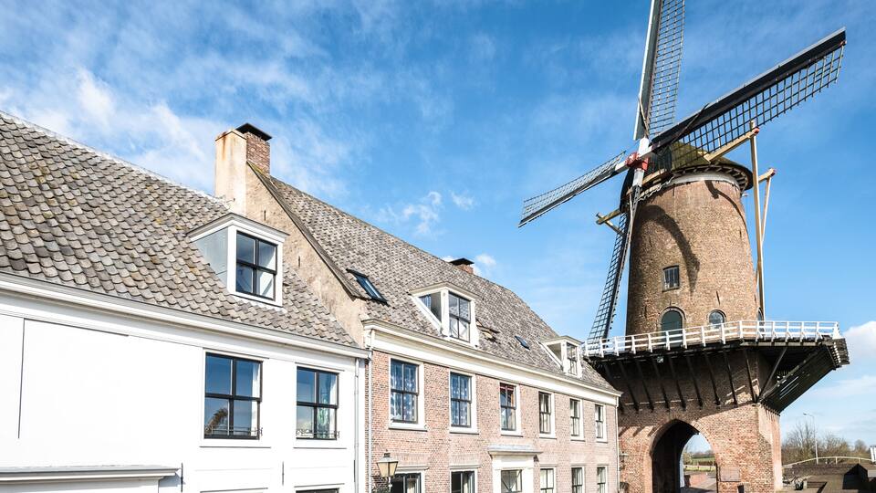 A traditional windmill with a brick tower and a white building with multiple windows.