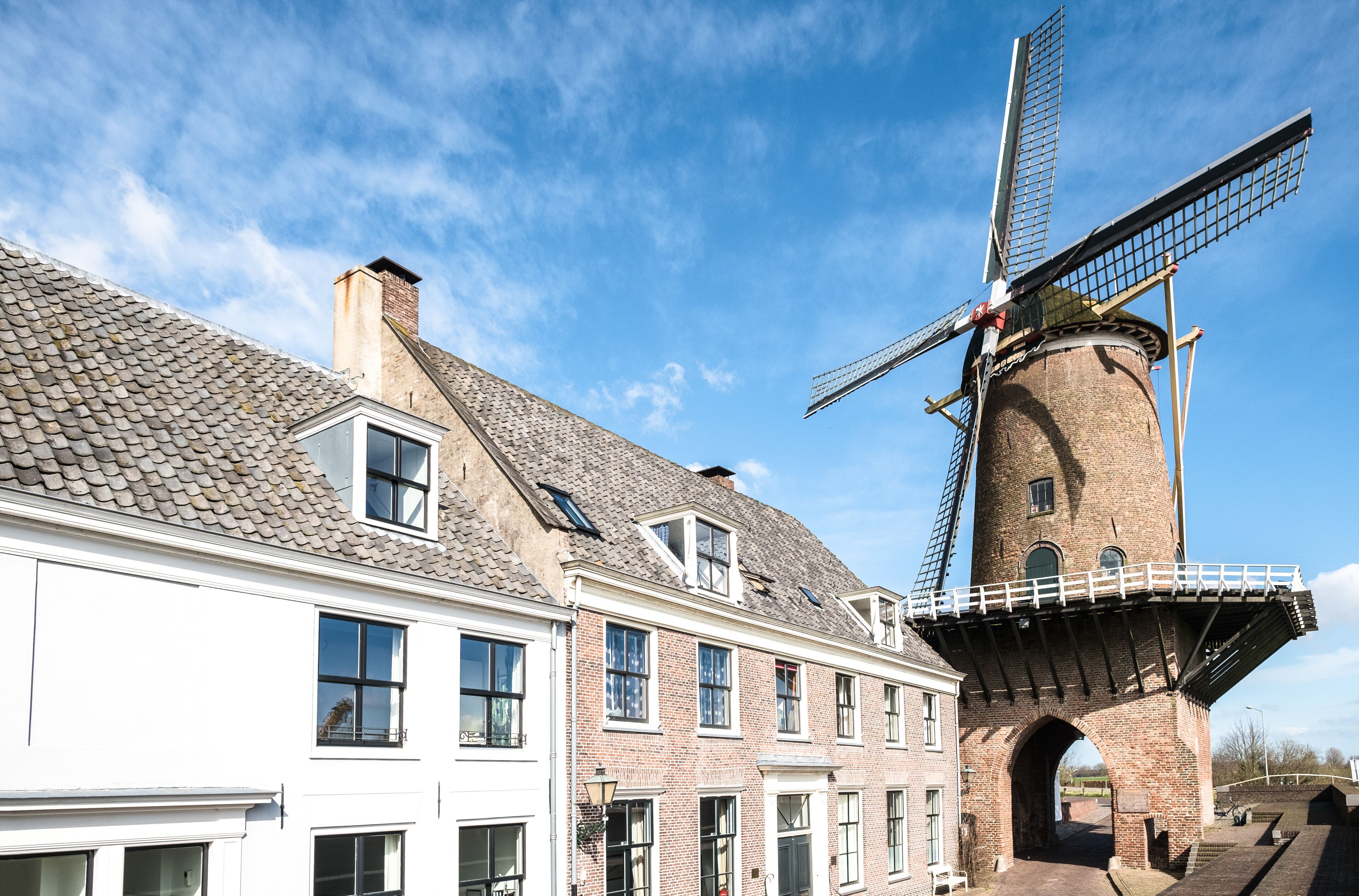 A traditional windmill with a brick tower and a white building with multiple windows.