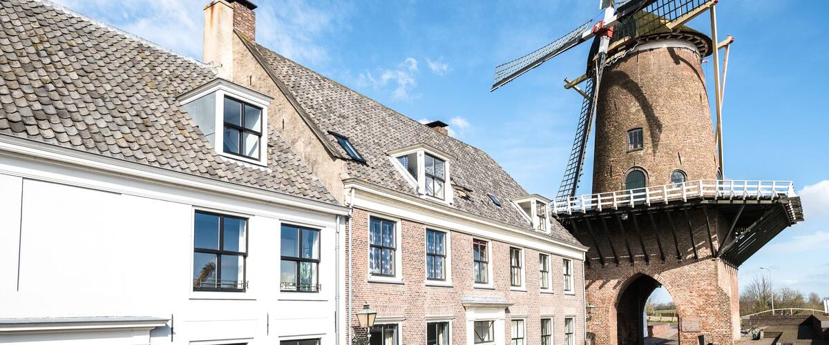 A traditional windmill with a brick tower and a white building with multiple windows.