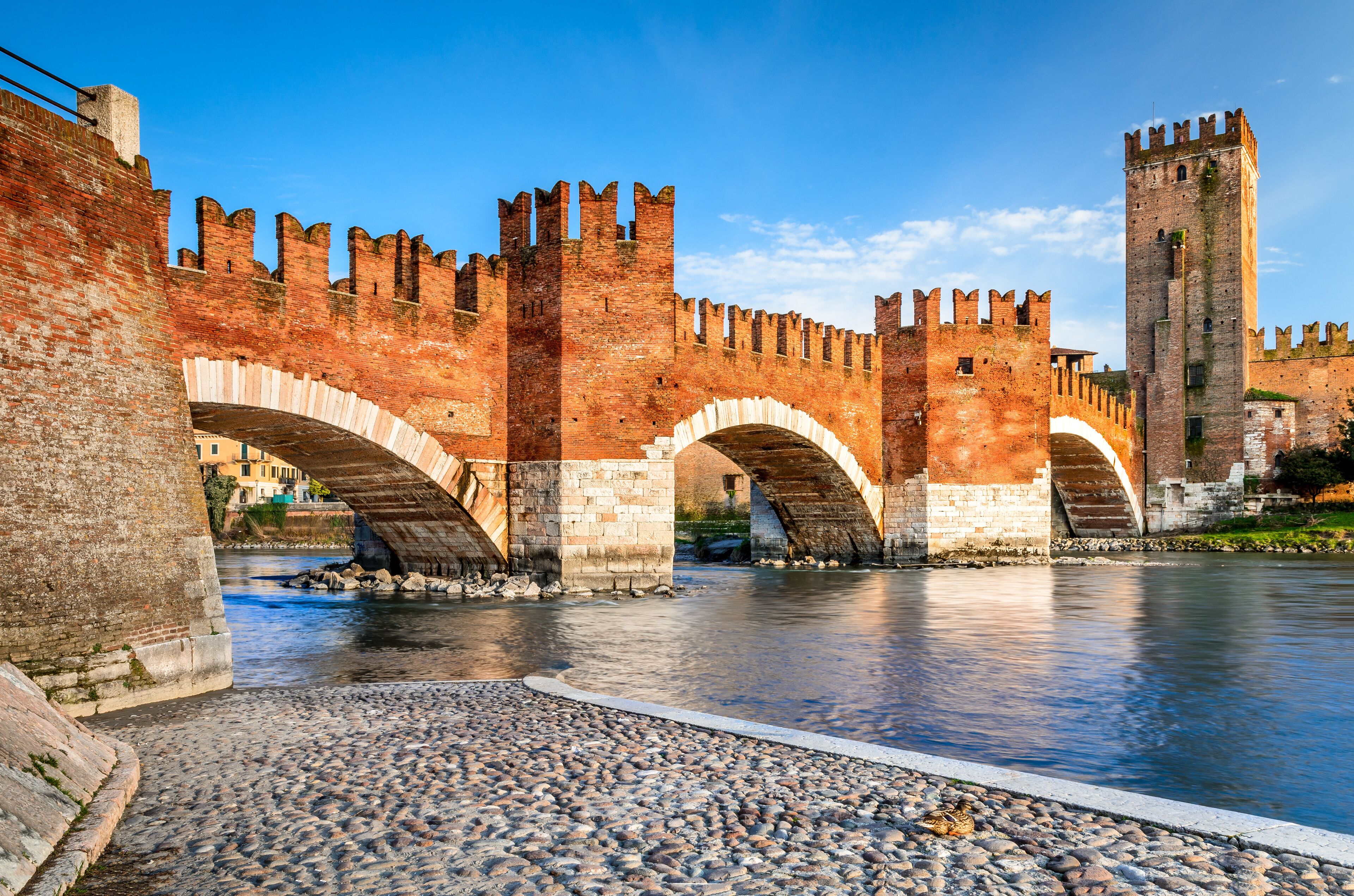 A historic stone bridge with arches over a river, surrounded by ancient brick walls and a tall tower.