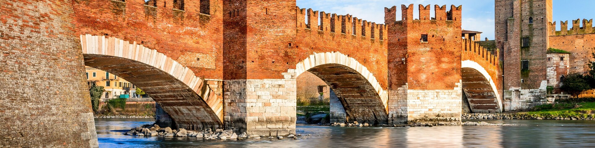 A historic stone bridge with arches over a river, surrounded by ancient brick walls and a tall tower.