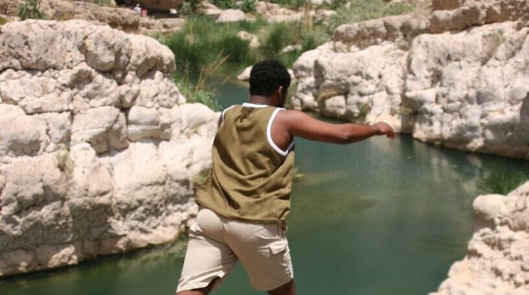 Wadi Shab is a truly magical place that is made even more amazing with a little local knowledge. To get there from Muscat, no 4WD required. Head along the road to Sur and not long after Fins Beach, take a turn off (slipway) to the right for Wadi Shab or Tiwi Village - it is signposted. Head down under the road and turn left to go underneath the highway. When you come out from under the bridge, do not turn immediately right, cross this road and turn right immediately after it. Follow this road through the village and down the steep hill to the causeway. When you cross over the causeway, turn right and park under the highway.
Once you have reached here, you need to take a boat across to the other bank in order to walk up the Wadi. It costs 300 baisa (about 80 US cents). Try to have small change for this - you would be lucky if these guys carried change for a 10, let alone anything bigger. Check what time the last boat goes back - it changes with the season.
Once you are across, there is a long but rewarding walk ahead. Luckily there are lots of stunning pools to take a dip in along the way. In 2012, Red Bull held the finals of the Cliff Diving Championships here. Eventually, the walk kind of stops at the water's edge. There is just a rock wall in front of you and a beach of smooth rock to enter the wadi. This is where it is time to get wet. You will need a waterproof bag if you are carrying valuables and I strongly recommend water shoes of some kind.
Keep following the wadi upstream. There will be some climbing over rocks and up small gravelly waterfalls and some swimming. How much will depend on the current water level.
You will reach a rock wall in front of you and the wadi just seems to appear out of it. There are now only 2 ways to go - back where you came from - or through the wall. There is a crack in the middle of the wall. Go to where this "meets" the water. If the water level is high, it will be all the way up and the only way through is to swim under rock. This is without a doubt dangerous going in blind and one of my least favourite things. I won't do this. If the water level is low enough, which it always has been for me, you can "swim" under, with enough room to get your head through, so you can both see and breathe - a much safer option. You can use your hands on the rock to propel you through.
What do you do all of this for...? You are now in a cave with a waterfall. It is partially open at the top, so it is shady rather than dark and the locals have fixed a rope up through the waterfall so you can climb up and jump in. With so many other options further down river for jumping in or stopping in the shade by the water, this may seem like a lot, but it is truly beautiful.
Note: Take plenty of drinking water, sunscreen, hat and energy food. It is warm even in winter - especially if you are from colder climes.
But most of all - enjoy! And don't be surprised if there are some local lads around eager to show you the way!