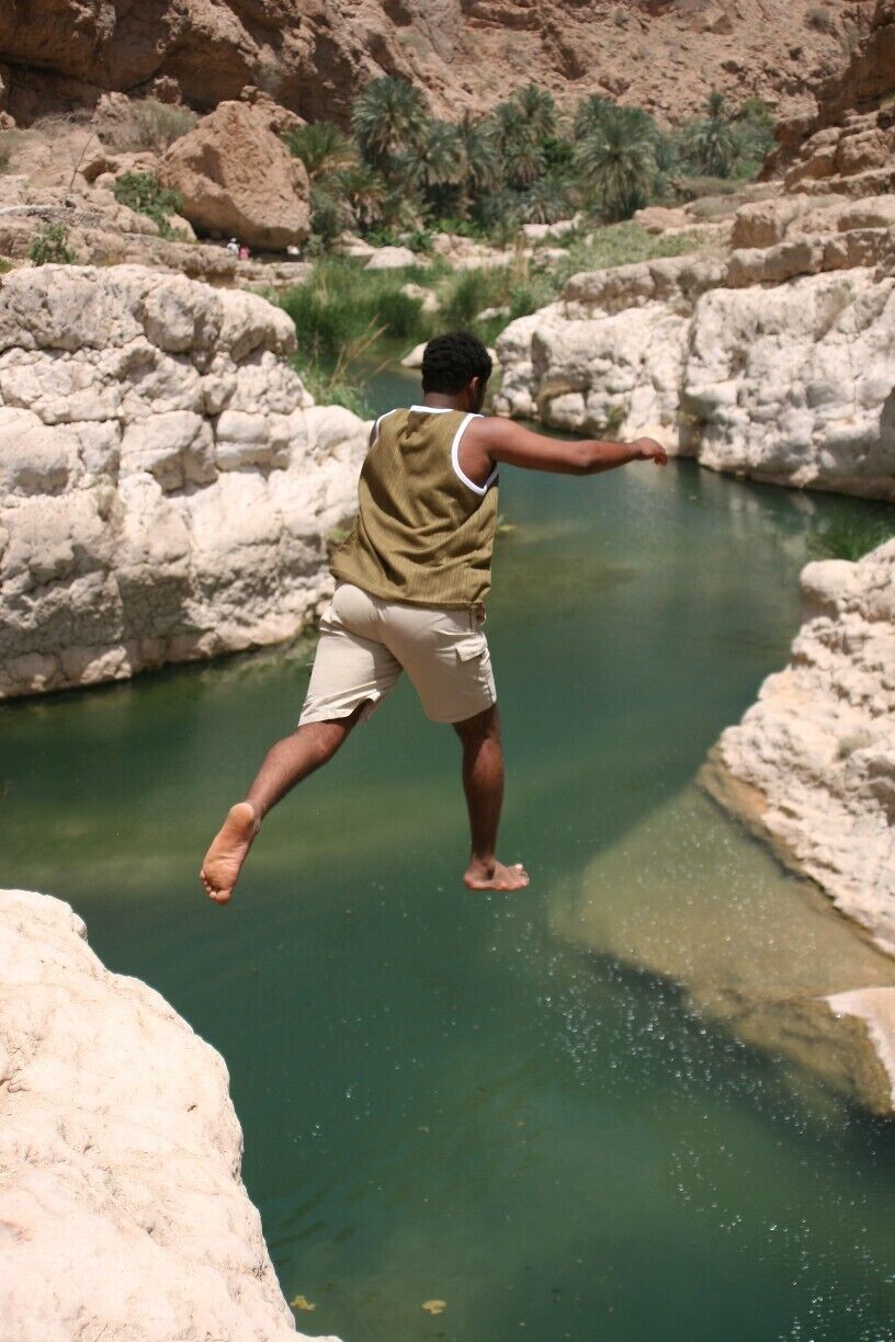 A person jumping into a clear water body surrounded by rocky terrain.