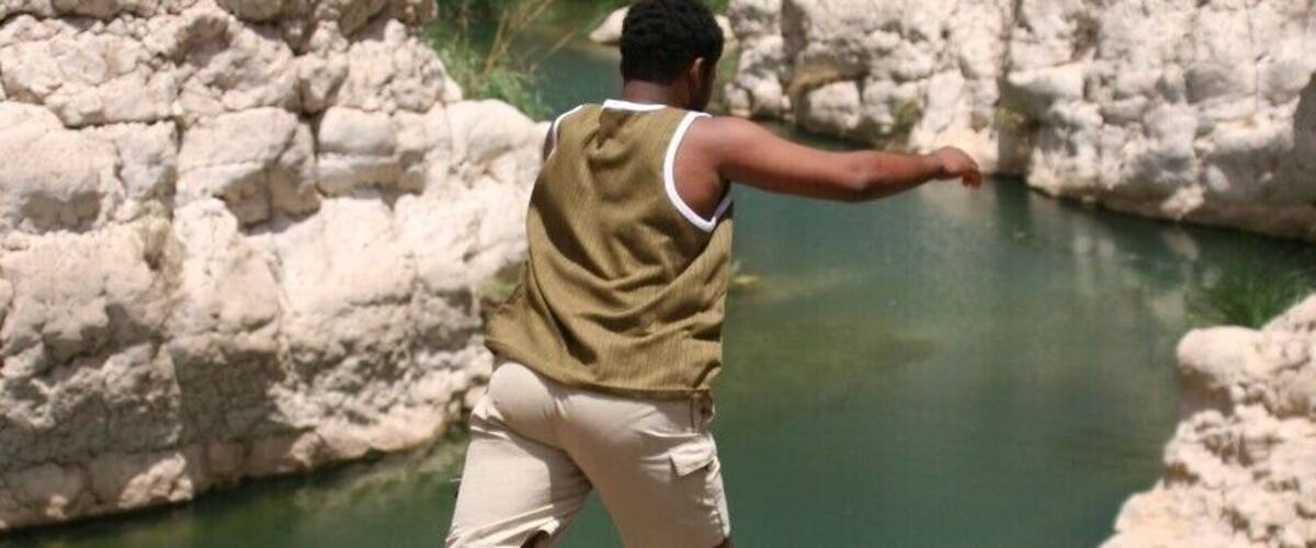 A person jumping into a clear water body surrounded by rocky terrain.