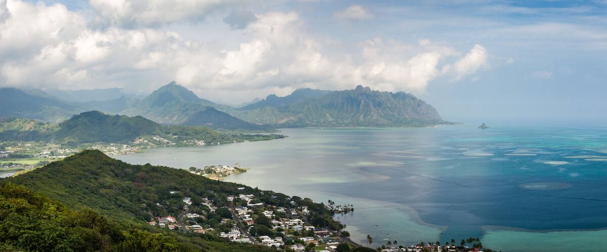 A coastal landscape with a mountain range, a town, and a clear blue sea.
