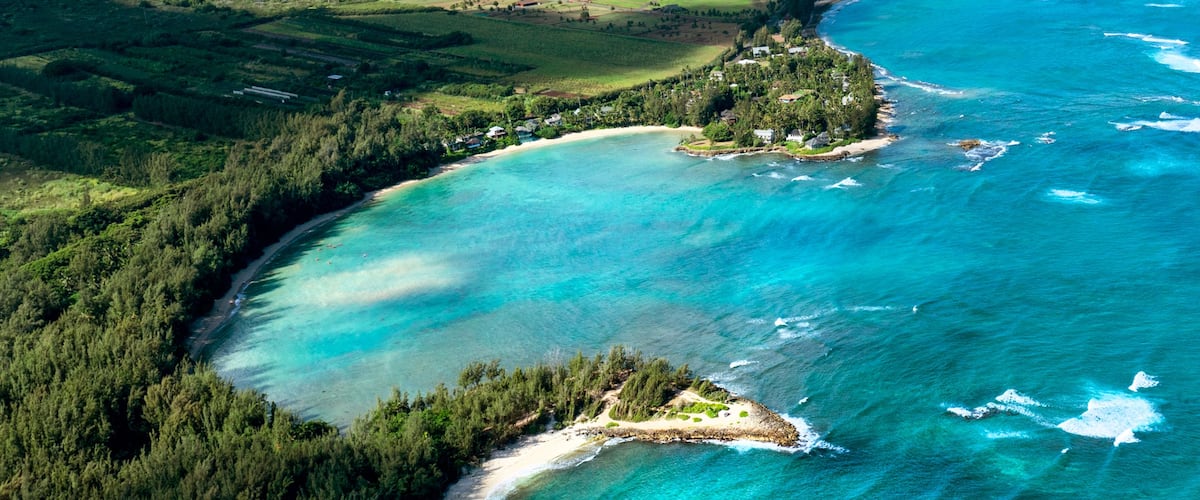 A coastal landscape with a clear turquoise sea, sandy beaches, and a forested area.