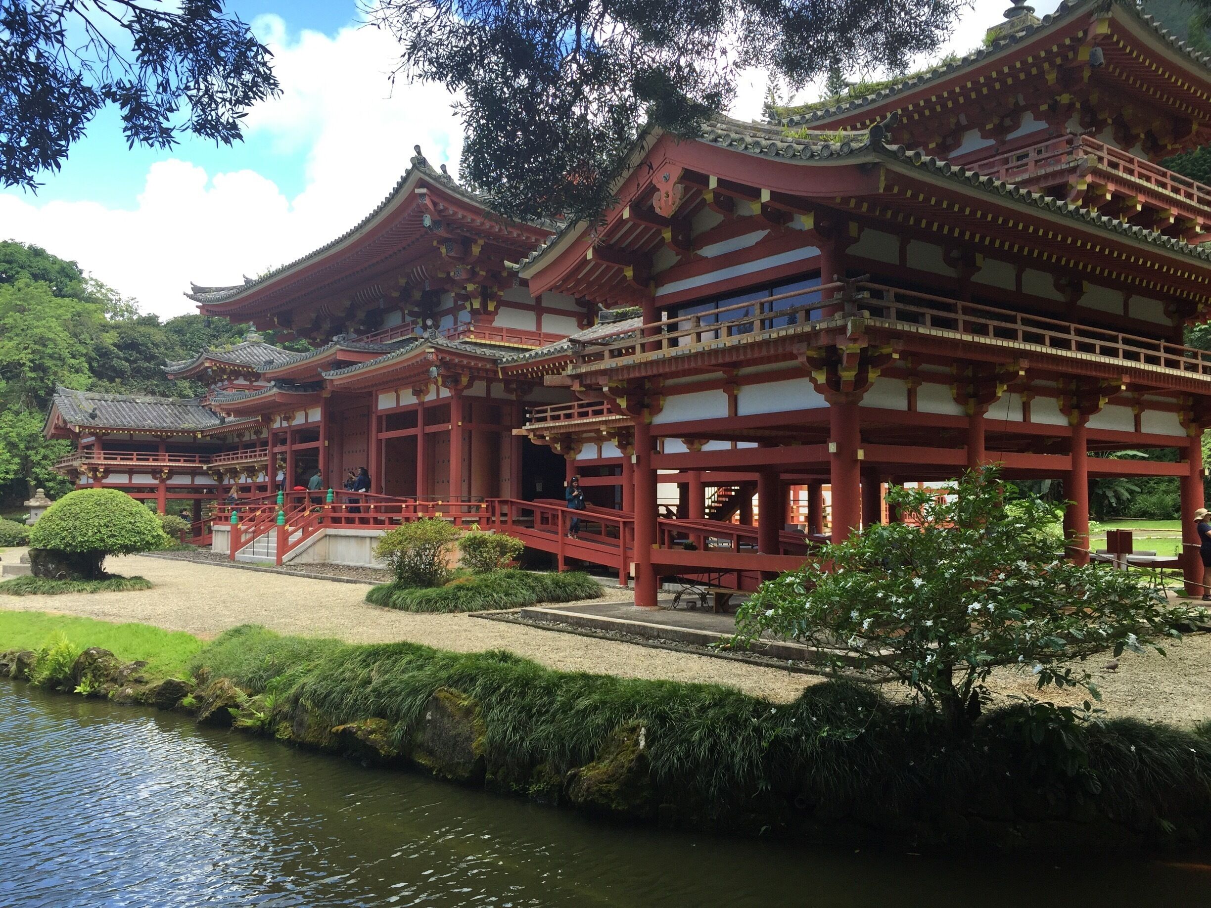 Ett traditionellt japanskt tempel med flera byggnader som har röda tak, en stig av sten och en damm.