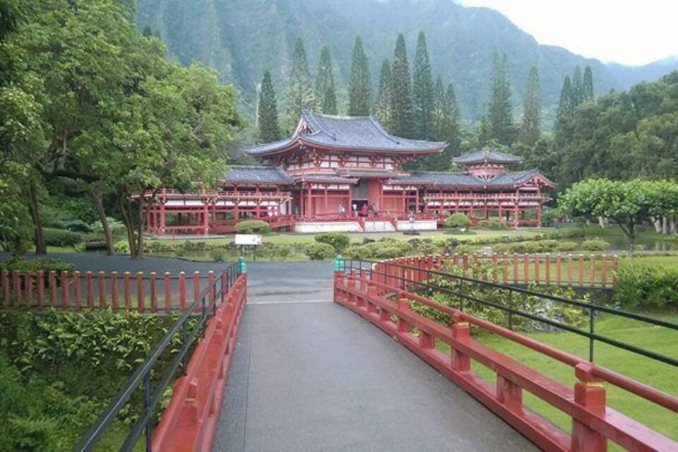 A traditional Japanese temple with a red bridge leading to it, surrounded by lush greenery and mountains in the background.