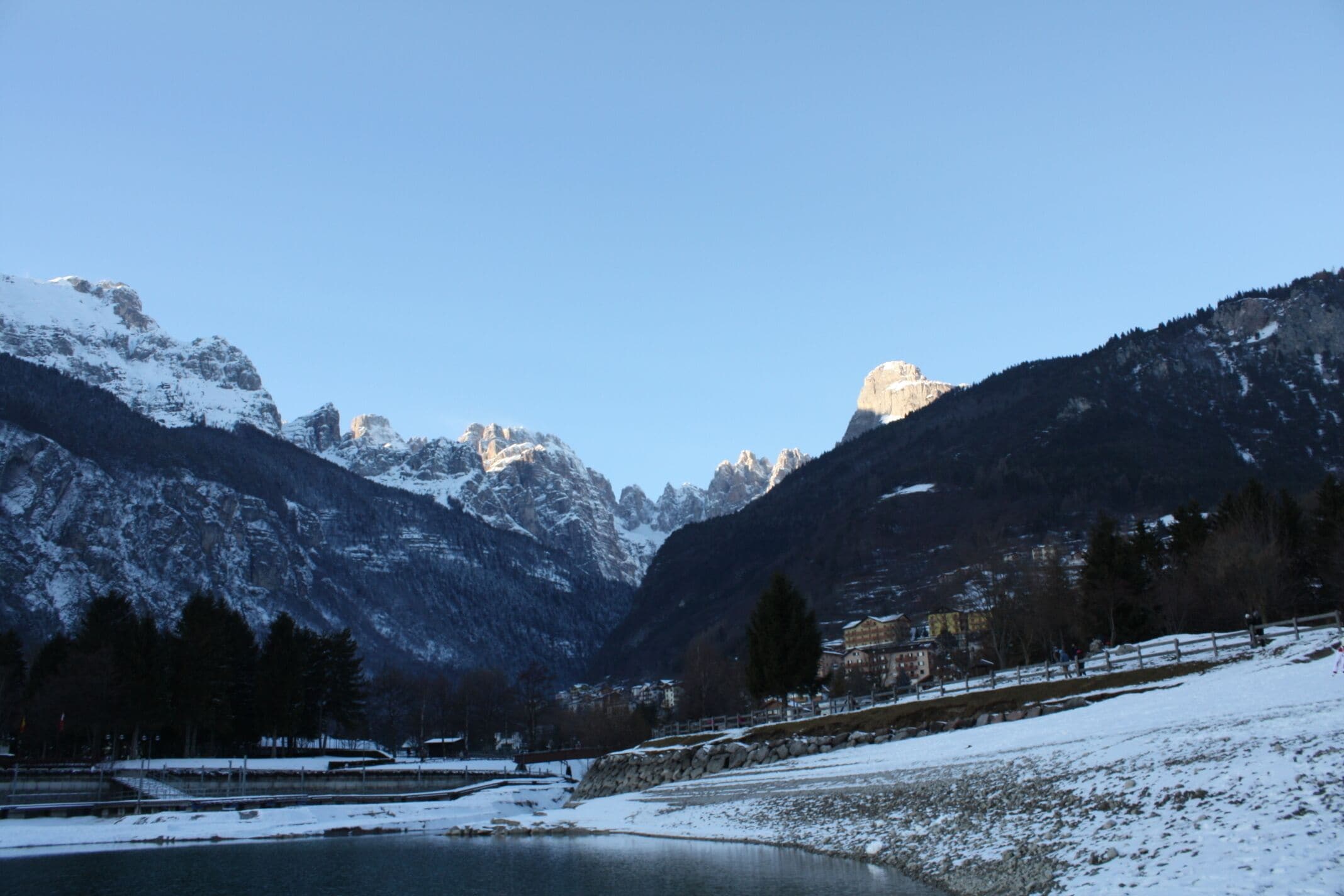 A snow-covered landscape with mountains, a lake, and a building in the valley.