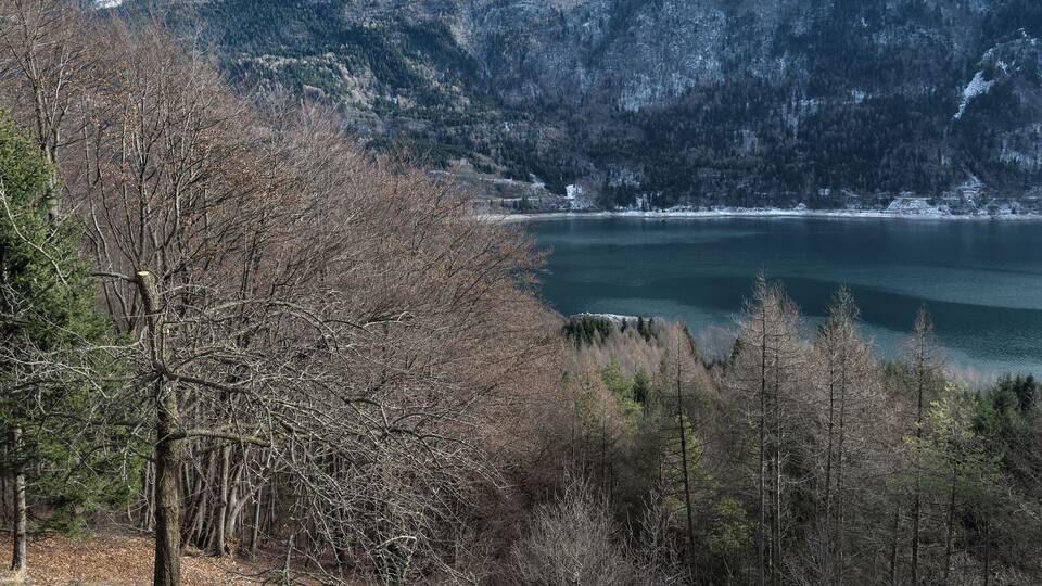 A mountainous landscape with a lake, trees, and a clear sky.
