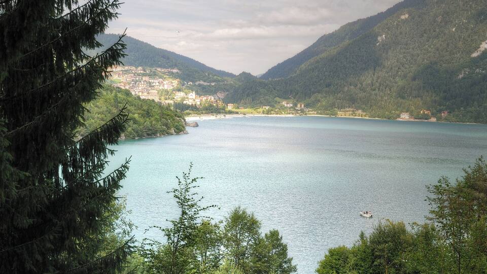 A lake surrounded by mountains, trees, and a small town in the distance.