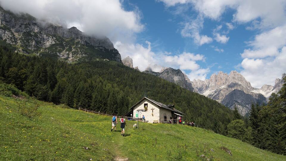 A mountain landscape with a wooden cabin, a path, and hikers.
