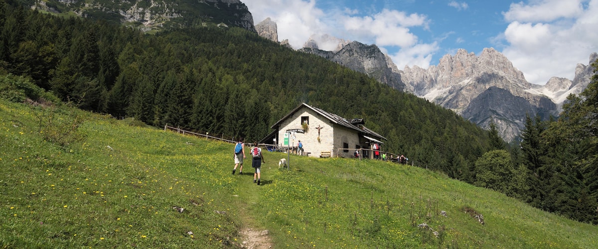 A mountain landscape with a wooden cabin, a path, and hikers.