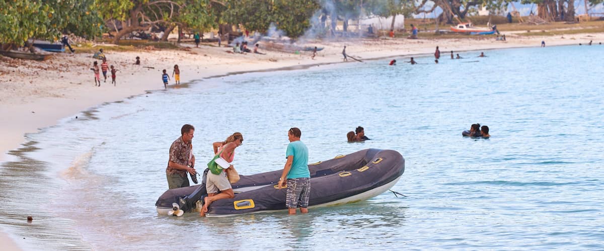A beach scene with people on a raft, a sandy shore, and trees in the background.