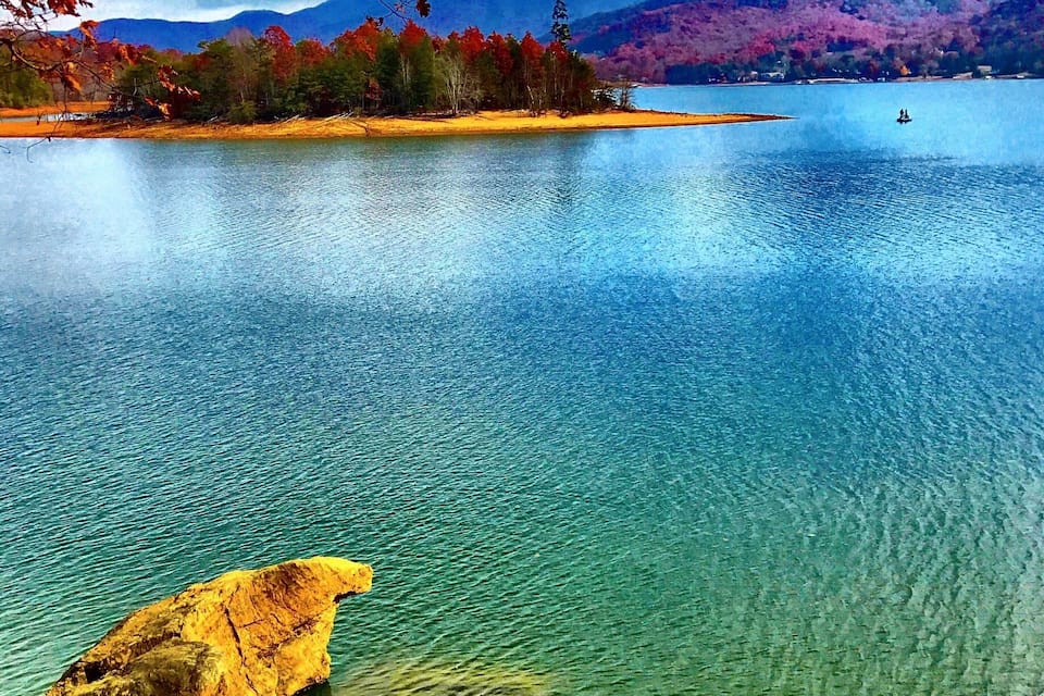 A lake with clear water, autumn leaves, and mountains in the background.