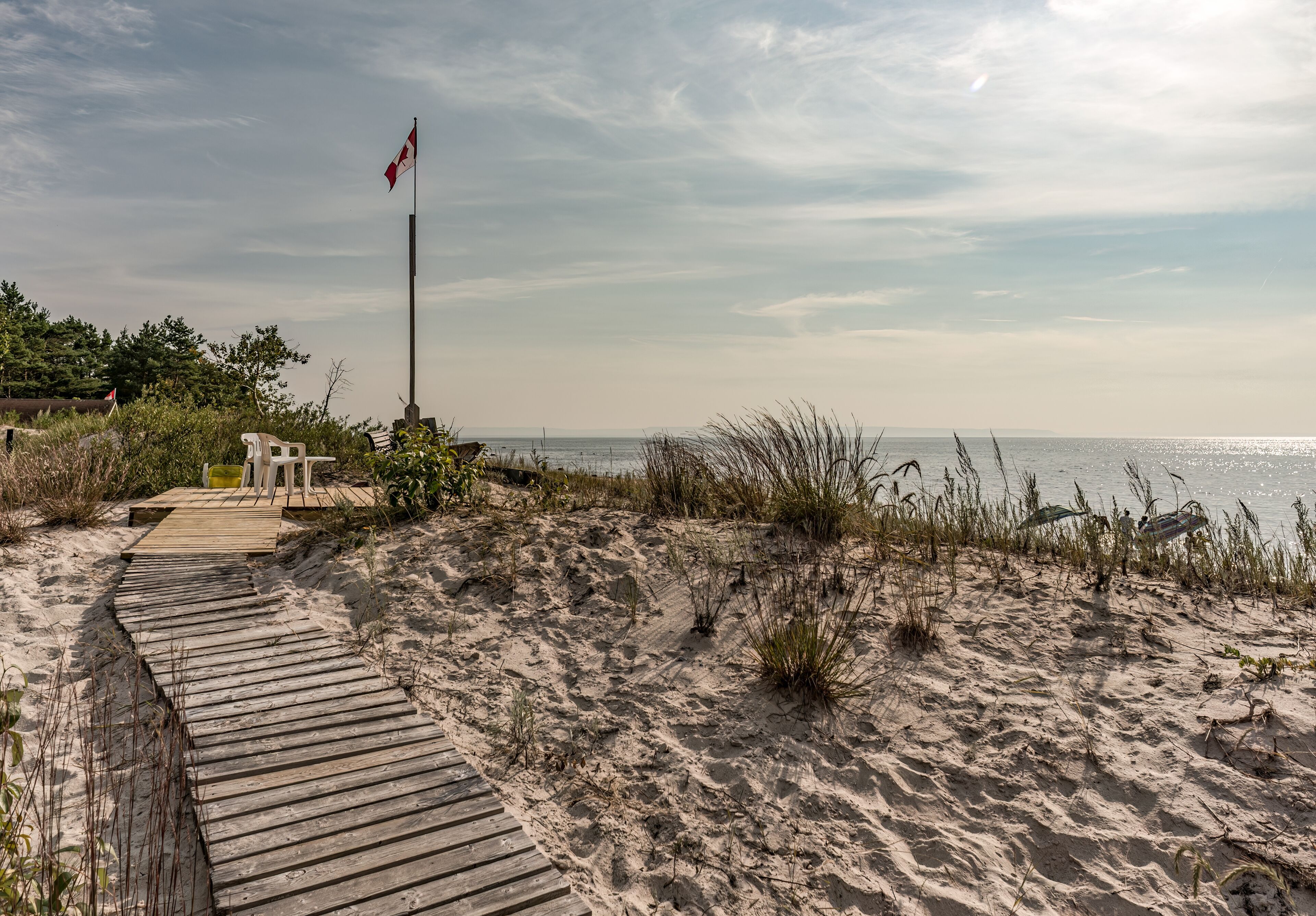 Bluewater Beach, Tiny Township, Ontario, Canada - August 10, 2014: A boardwalk across the dunes leads to a platform with seating and a flag overlooking Georgian Bay on a sunny summer morning