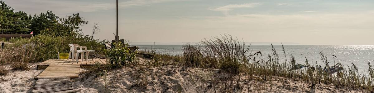 A wooden boardwalk leading to a flagpole with a flag, surrounded by sand dunes and sparse vegetation.