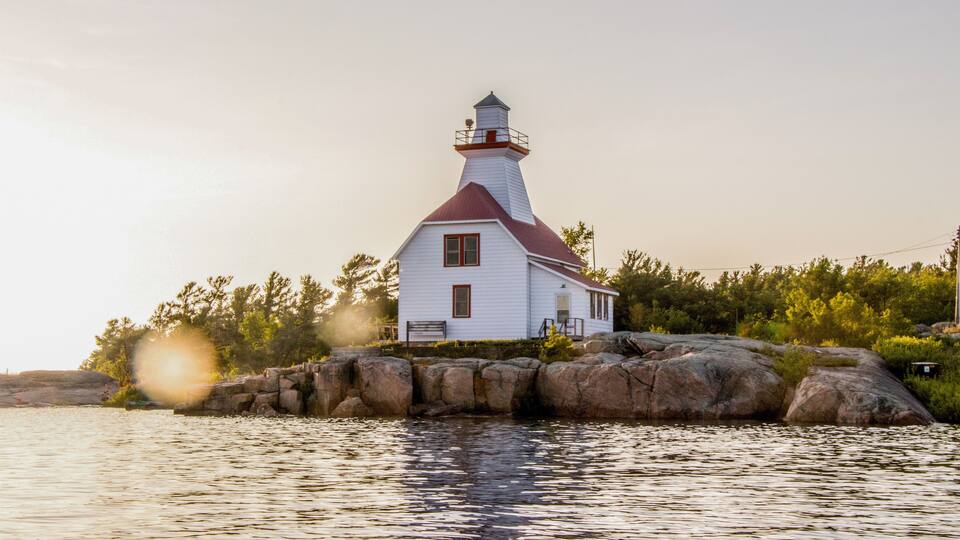 A white lighthouse with a red roof on a rocky island surrounded by calm water.