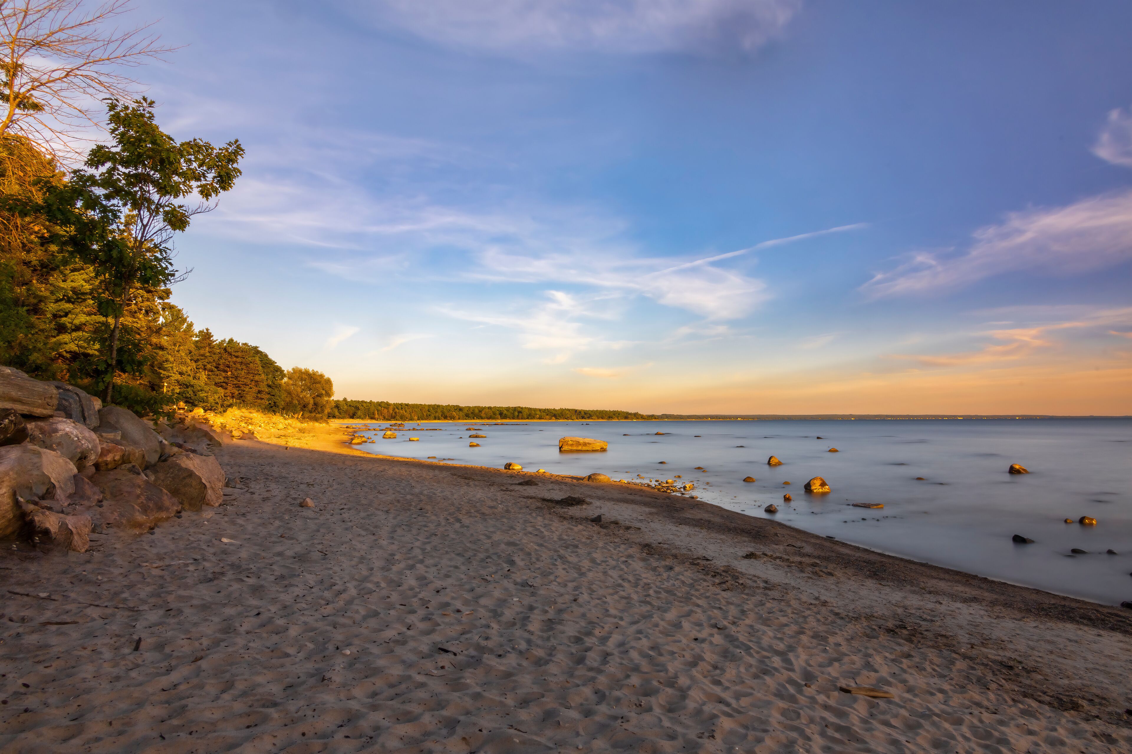 A stunning sunset over a serene beach in Tiny, Ontario, capturing the tranquil beauty and vibrant colors of the evening sky reflecting on the calm waters.
